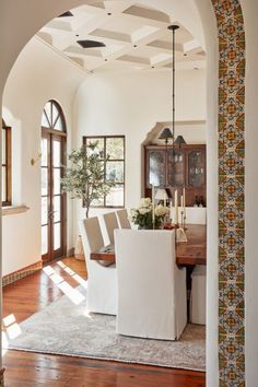 a dining room table and chairs with an archway leading to the living room, which is decorated in white