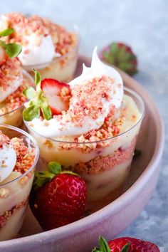 three desserts with strawberries and whipped cream in a pink bowl on a table