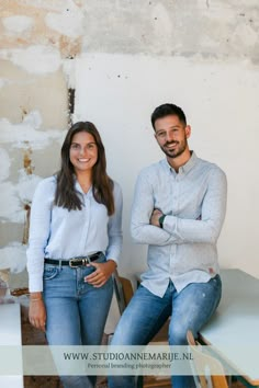 a man and woman sitting next to each other in front of a wall with peeling paint