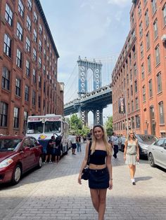 a woman is walking down the street in front of some tall buildings and a bridge