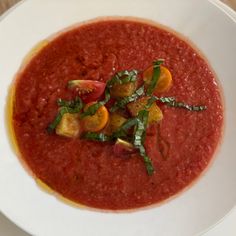 a white plate topped with a red soup and garnished with veggies