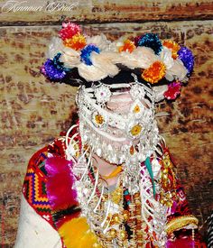 a man with long white hair wearing a colorful headdress and flowers in his hair