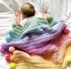 a baby laying on top of a bed next to a multi colored crocheted blanket