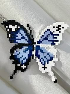 a blue and black butterfly is hanging from a hook on a white curtain with it's wings spread out