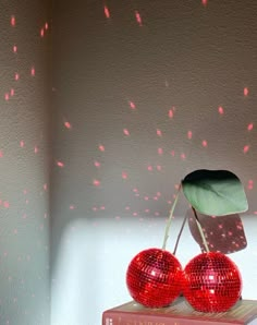 two shiny red disco balls sit on top of a book with a green leaf sticking out of it