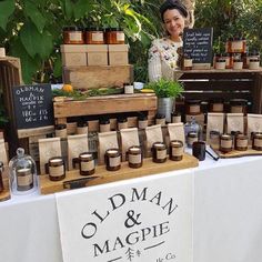 a woman standing behind a table with jars and bottles on it that are labeled old man & magpie