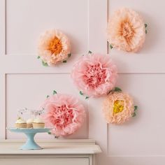 three pink flowers are on the wall next to a cake stand and cupcakes