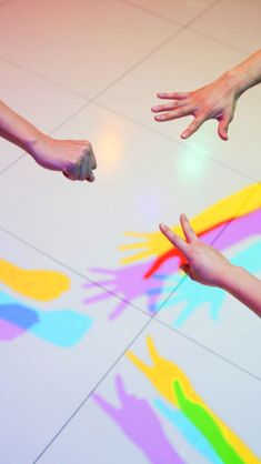 two hands reaching out towards each other on a floor with multicolored paint designs