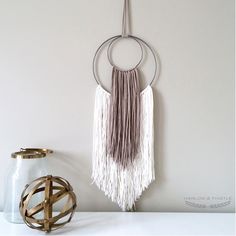 a wall hanging with two rings and tassels on it next to a vase