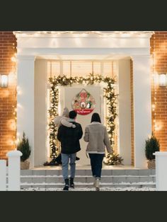 two people are walking into the front door of a house decorated with christmas lights and garlands