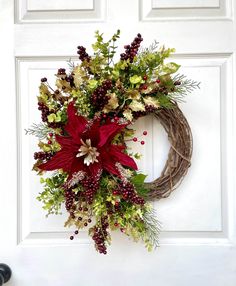 a wreath with red flowers and greenery hangs on the front door's white door