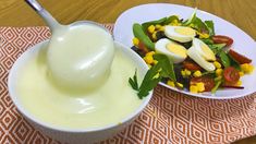 a white bowl filled with salad and dressing next to a plate of boiled eggs on a wooden table