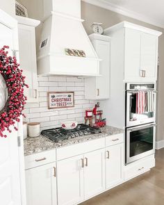 a kitchen with white cabinets and christmas decorations on the stove top, along with a wreath