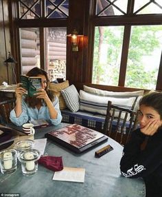 a woman sitting at a table with a book in front of her and another person reading