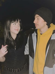 a man and woman standing next to each other in front of a tree at night