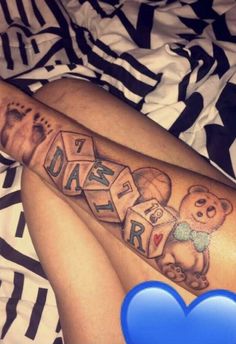 a person laying on top of a bed with a teddy bear and letters tattooed on their leg