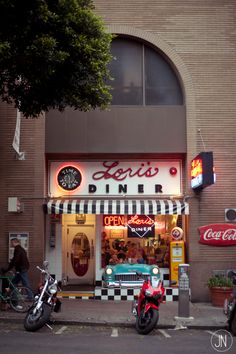 two motorcycles parked in front of a diner with neon signs on the side of the building