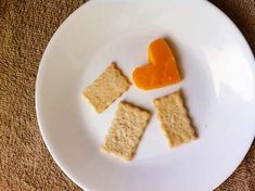 some crackers are on a white plate with an orange heart shaped candy in the middle