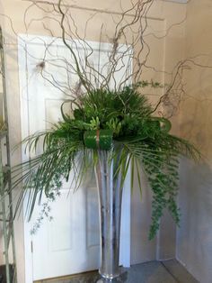 a tall metal vase filled with lots of greenery next to a white door way