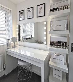 a white vanity with lights on it next to a large mirror and shelf filled with cosmetics