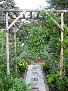 a garden with lots of green plants and flowers on the sides of it, along with a brick walkway