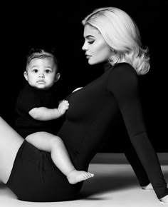 a woman is holding a baby in her lap and posing for the camera with black background