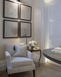 a white chair sitting next to a table in a room with pictures on the wall