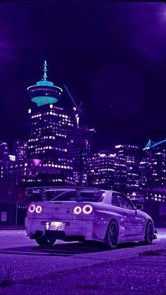 a purple car parked in front of a city skyline at night with the lights on