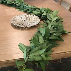 a wooden table topped with green leaves and a white bowl on top of the table