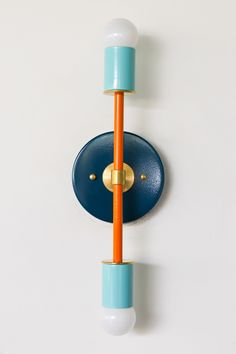 an orange and blue wall light with two lights on it's sides next to a white wall