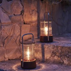 two lights that are sitting on some stone steps in front of a rock wall, one is lit up and the other is turned on