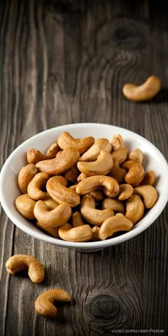 a white bowl filled with cashews on top of a wooden table