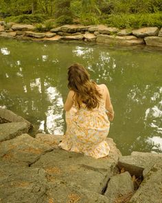 a woman sitting on some rocks by the water with her back turned to the camera