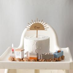 a white cake sitting on top of a table with toy train cars and a wooden one sign