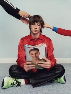 a man sitting on the floor while holding a magazine with his face in front of him