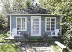 a small gray and white house with two chairs on the front porch next to it