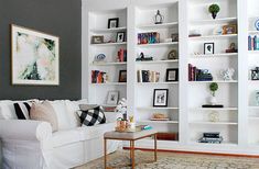 a living room filled with lots of white bookshelves next to a couch and coffee table