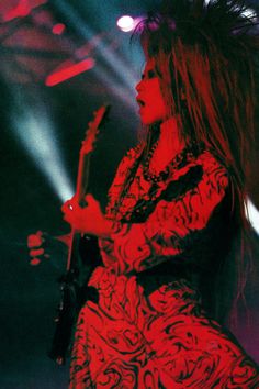 a woman with long hair holding a guitar in front of some bright colored lights at a concert