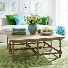 a living room filled with furniture and green pillows on top of a white couch next to a coffee table