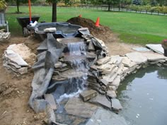 an outdoor pond with rocks and water flowing from it's sides to the ground