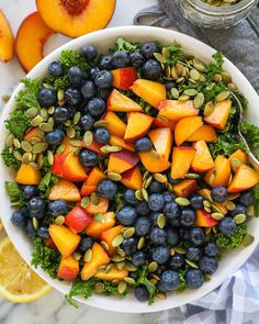 a white bowl filled with blueberries, peaches and pistachio on top of a marble table