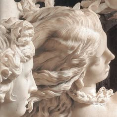 two white statues with curly hair and flowers on their heads, one is looking at the other