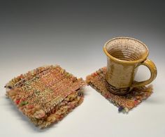 two coffee mugs sitting next to each other on top of a cloth covered table