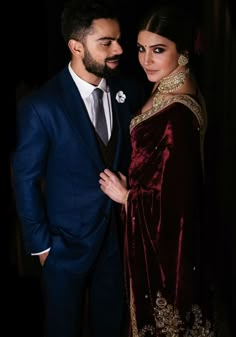 a man in a suit and tie standing next to a woman wearing a red velvet dress