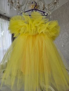 a yellow dress hanging on a hanger in front of a chandelier and curtains