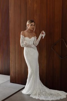 a woman in a white wedding dress standing next to a wooden wall with her hands on her hips