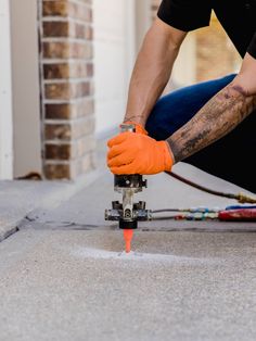 a man in orange gloves is using a drill to fix a hole on the ground