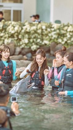 several women in life jackets are standing in the water and talking to someone on their cell phone