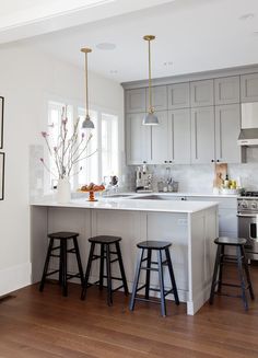 a kitchen with three stools in front of an island and two lights above it