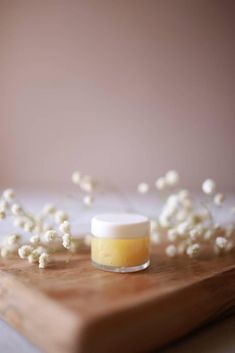 a wooden cutting board topped with white flowers and a jar of lip balm sitting on top of it